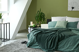 Bettwäsche für jede Jahreszeit: Ein helles Schlafzimmer mit grünen Pflanzen und einem Doppelbett, das mit weißer Bettwäsche mit einem grünen Rankenmuster überzogen ist.