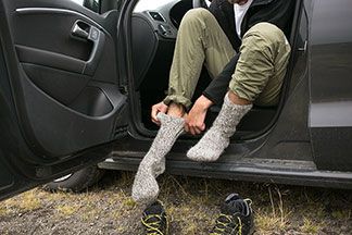 Nahaufnahme eines Mannes, der im Auto sitzend seine Sportsocken anzieht, um eine Wanderung zu starten.