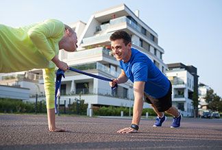 Einfaches Fitnessgerät: Ein junges Pärchen macht gemeinsam eine Übung mit einem Thera-Band auf einer ruhigen Straße in urbaner Umgebung.