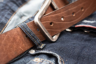 Herren-Accessoires als Hingucker: Nahaufnahme eines braunen Ledergürtels an einer Jeans.