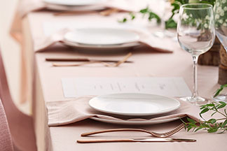 Eine feierlich dekorierte Tafel, mit einer rosa Leinentischdecke. Der Tisch ist mit schlichten Tellern und Kupfer-Besteck gedeckt.