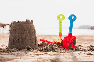Viel Spaß mit Spielzeug für draußen: Eine Sandburg am Strand neben der zwei kleine Plastikschaufeln im Sand stecken.