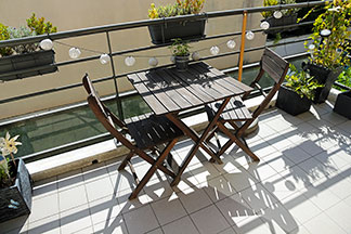 Gartenstühle für den Balkon: Auf einem kleinen Balkon stehen zwei Holzstühle und ein viereckiger Holztisch.