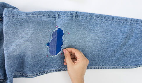 Ein Hosenloch einer Jeans wird mit Stecknadeln abgesteckt