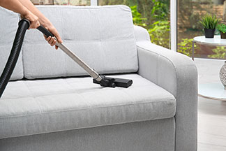 Ein graues Sofa wird mit einem Staubsauger gereinigt.