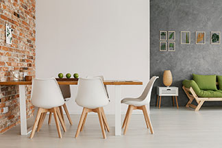 Ein modern eingerichtetes Wohnzimmer mit einem Esstisch, an dem weiße Schalen-Stühle mit hellen Holzbeinen stehen.