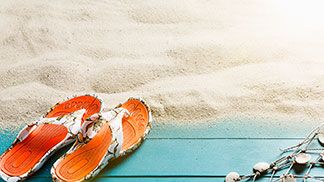 Orangene Zehentrenner im Sand am Strand: Bei Tchibo finden Sie nicht nur Bikinis und Co., sondern auch passende Accessoires für den Badeurlaub.