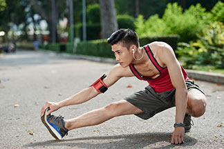 Ein junger, sportlicher Mann in Sportswear und mit Sportschuhen beim Stretching in einem Park.