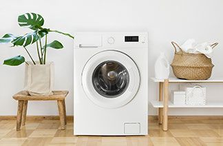 Funktionswäsche richtig waschen: Ein Waschraum in dem eine Waschmaschine sowie ein Wäschekorb und ein Regal stehen.
