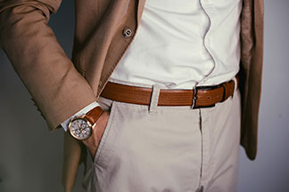 Accessoires richtig kombinieren: Nahaufnahme eines Mannes, der eine Uhr mit einem braunen Lederarmband, einen farblich passenden Gürtel sowie ein passendes Sakko trägt.