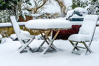 Gartenmöbel richtig überwintern: Ein stark verschneiter Tisch und zwei Stühle einer Terrasse im Winter.