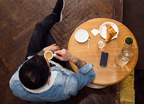Ein Mann trinkt in Jeans und Jeans-Jacke gekleidet Kaffee in einem Café