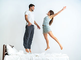 Gute Laune am Morgen: ein Vater liegt auf dem Rücken im Bett und hebt seine kleine Tochter mit ausgestreckten Armen in die Luft.