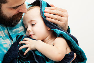 Gütesiegel schafft Vertrauen: Ein Vater hält sein Baby im Arm, das in ein blaues Handtuch gewickelt ist.