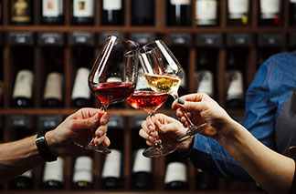Für jeden Wein das ideal Glas: Verschiedenen Weingläsern beim Anstoßen vor einem Weinregal.