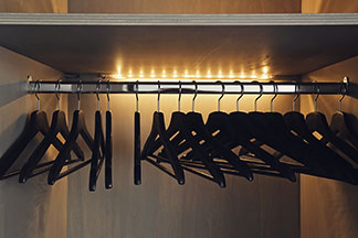 Schranklampen bei Tchibo in guter Qualität: Eine Kleiderstange in einem dunklen Holzschrank mit leeren Kleiderbügeln – beleuchtet von einem Lichtstreifen an der Rückwand.