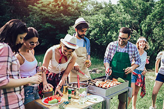 Auch Gemüse kann auf den Grill: Eine Gruppe junger Leute steht am Grill, und bereitet zusätzlich an einem kleinen Tisch Gemüse zu.