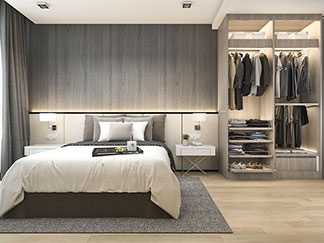 Gute Qualität für Ihren Schlafzimmerschrank: Blick in ein Schlafzimmer, in dem links das Bett steht, rechts ein offener Schlafzimmerschrank aus grau lasiertem Holz.