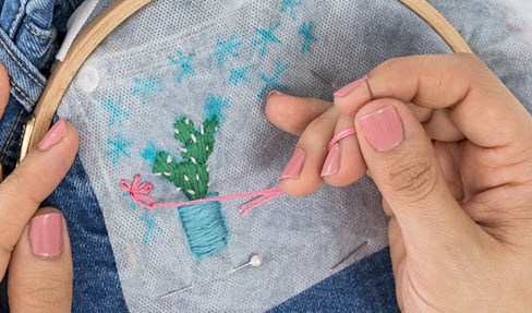 Eine Nadel wird mit einem rosa Faden durch eine Jeans und ein weißes Vlies geführt