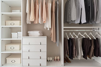Aufbewahrung im Kleiderschrank: Ein offener Kleiderschrank in dem Hemden und Hosen sowie Blusen und Kleider auf Bügeln hängen – links auf Regalböden stehen verschiedene Ordnungsboxen.