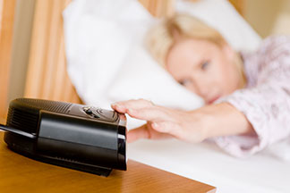 Gut gelaunt aufwachen: Eine Frau liegt im Bett und schaltet ihren Radiowecker aus, der auf dem Nachttisch steht.