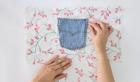 Die Gesäßtasche einer Jeans wird auf einen Stoff mit Blumenmuster aufgenäht