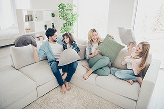 Platz für die ganze Familie: Ein Elternpaar sitzt mit ihren zwei Kindern auf einem weißen gemütlichen Big Sofa.