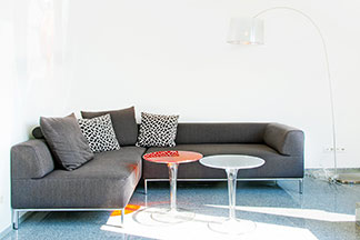 Wohnraum ideal nutzen: Ein graues, modernes Ecksofa mit zwei runden Tischchen und einer Stehlampe.