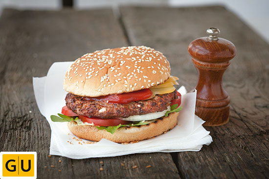 Klassischer Cheeseburger im Sesambrötchen angerichtet auf einer weißen Serviette mit holzfarbener Pfeffermühle.