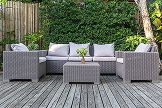 Loungemöbel für den Garten: Auf einer Holzterrasse steht eine graue Couch, ein Tisch und zwei Sessel, die mit weißen Kissen dekoriert sind.