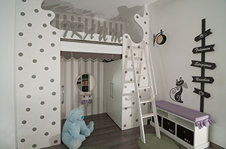 Stauraum und Sitzfläche: Ein weißes Lowboard, das im Kinderzimmer an der Wand steht, im unteren Bereich Schubfächer mit Kästen und eine lila Sitzauflage hat.