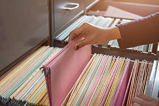 Eine Frauenhand sortiert Hängeregistermappen in die Schublade eines Büroschranks ein.
