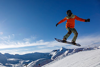 Sportjacken für den Winter: Ein Snowboarder bei einem Sprung in den verschneiten Bergen.