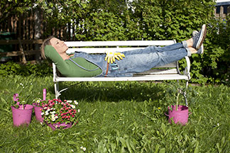 Sitzbank für draußen: Eine Frau liegt entspannt nach der Gartenarbeit auf einer weißen Bank im Garten.