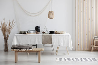 Ein Esstisch, auf dem eine Tischdecke aus Leinen liegt. Tisch und Wohnbereich sind in einem natürlich-rustikalen Stil gehalten, zu dem dieser Stoff bestens passt.