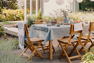 Einladender Essbereich im Freien: Auf einer Terrasse steht ein gedeckter Tisch mit einer blauen Tischdecke und fünf Gartenstühlen aus Holz.