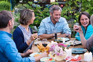 Gartenmöbel für gemeinsame Stunden: Sechs Erwachsene sitzen auf der Terrasse am Esstisch und unterhalten sich angeregt. Auf dem Tisch steht benutztes Geschirr sowie Weingläser.