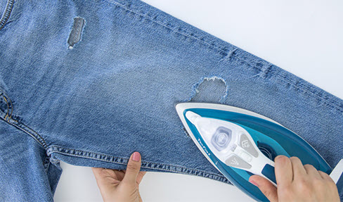 Ein Hosenloch einer Jeans wird glattgebügelt