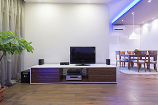 Praktische Abstellfläche: Ein edles Lowboard mit weißer Platte und dunklen Holzelementen auf dem ein Fernseher, kleine Boxen und weiter Multimedia-Geräte stehen.