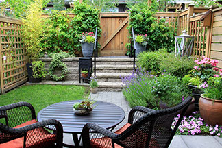 Gartenmöbel in guter Qualität: Auf einer kleinen Terrasse in einem Garten stehen zwei dunkle Gartenstühle mit roten Sitzkissen und Lehnen sowie ein Tisch.