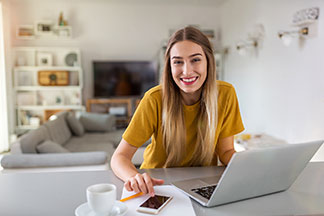 Arbeit von daheim: Eine junge Frau sitzt entspannt vor Ihrem Laptop an ihrem Arbeitsplatz im Home-Office.