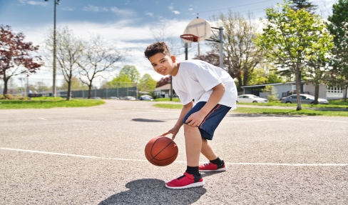Kind in Sportbekleidung spielt Basketball.