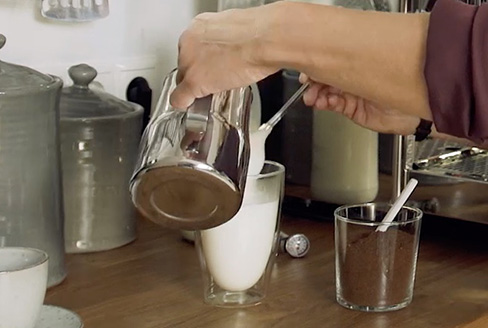 Milch wird in Latte Macchiato Glas gegossen
