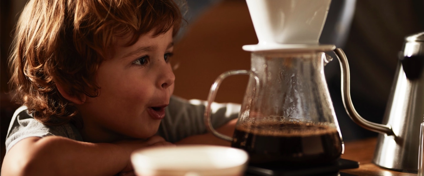Ein kleiner Junge schaut zu, wie ein Kaffee mit einem Keramikfilter in eine Glaskanne aufgebrüht wird. Das ist die Schwerpunkt Seite der Manuellen Zubereitung.