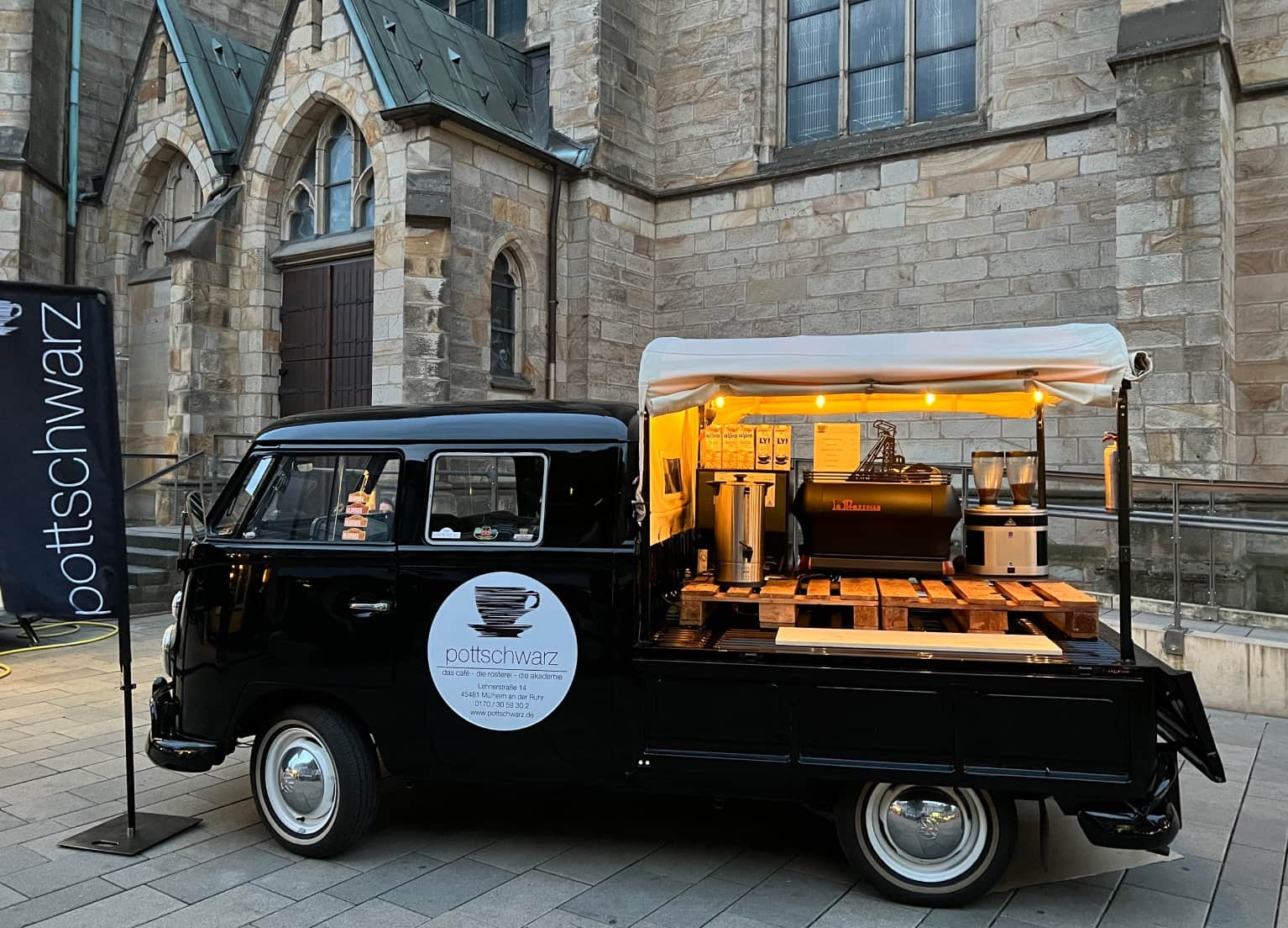 Kleines schwarzes Auto mit Kaffeebar hinten auf der Laderampe neben einer Flagge mit dem pottschwarz Logo