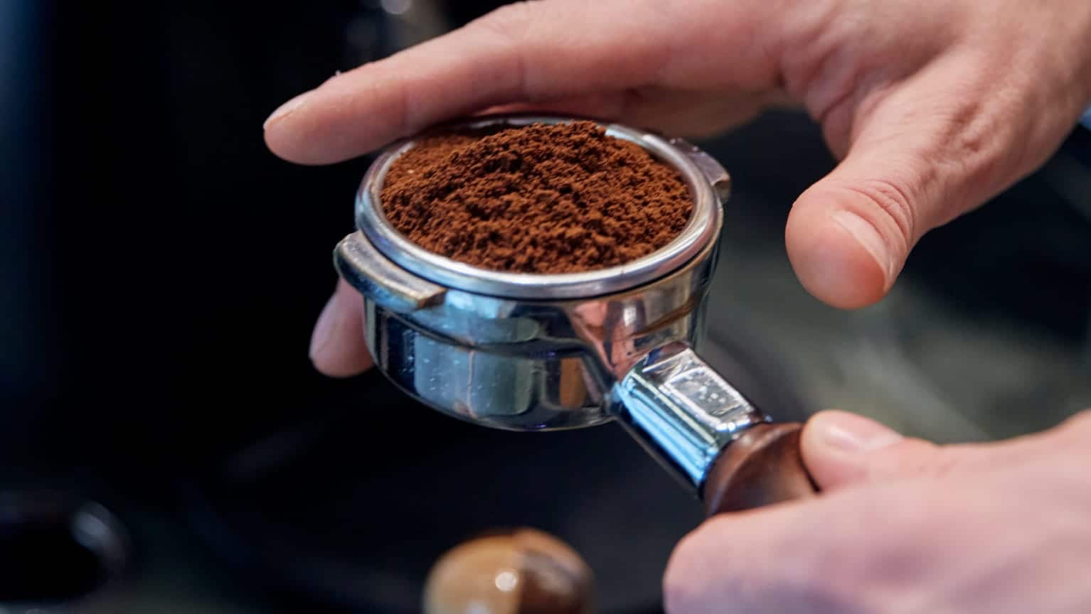 Nahaufnahme von einer Hand, die einen Siebträger mit Espressopulver hält