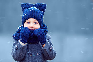 Kleiner Junge mit blauer Mütze und blauen Handschuhen im Schnee.